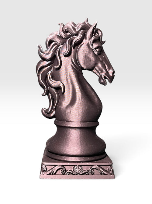 A knight chess piece statue shaped like a horse head with a flowing, ornate mane, standing on a square scrollwork base against a white to light grey gradient background.