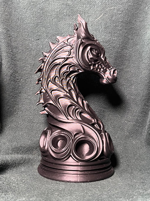 A knight piece statue shaped like a horse head wrapped in dragon scales, standing on a round base against a charcoal green fabric backdrop.