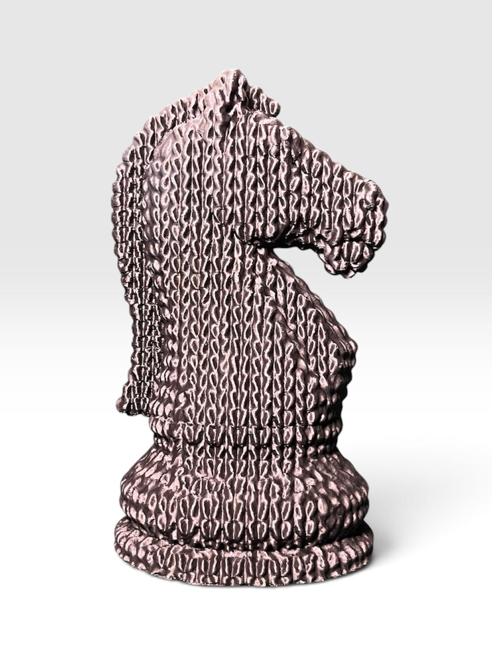 A knight chess piece statue shaped like a horse head sculpted with a knitted, stitched texture, standing on a round base against a white to light grey gradient background.
